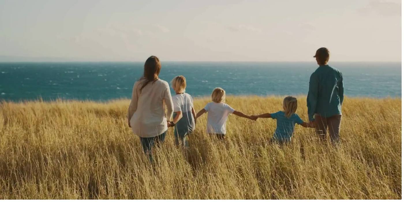 A family walking hand in hand through long grass by the sea