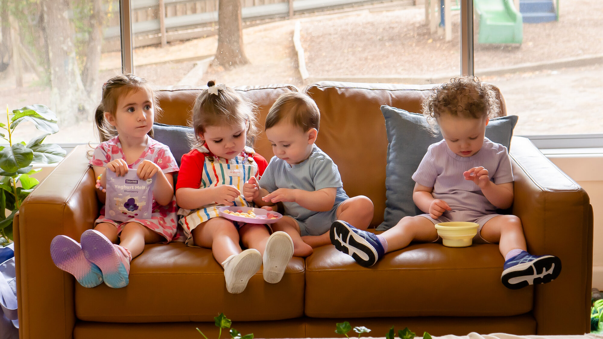 Four toddlers on a sofa sharing NaturKidz Yoghurt Melts